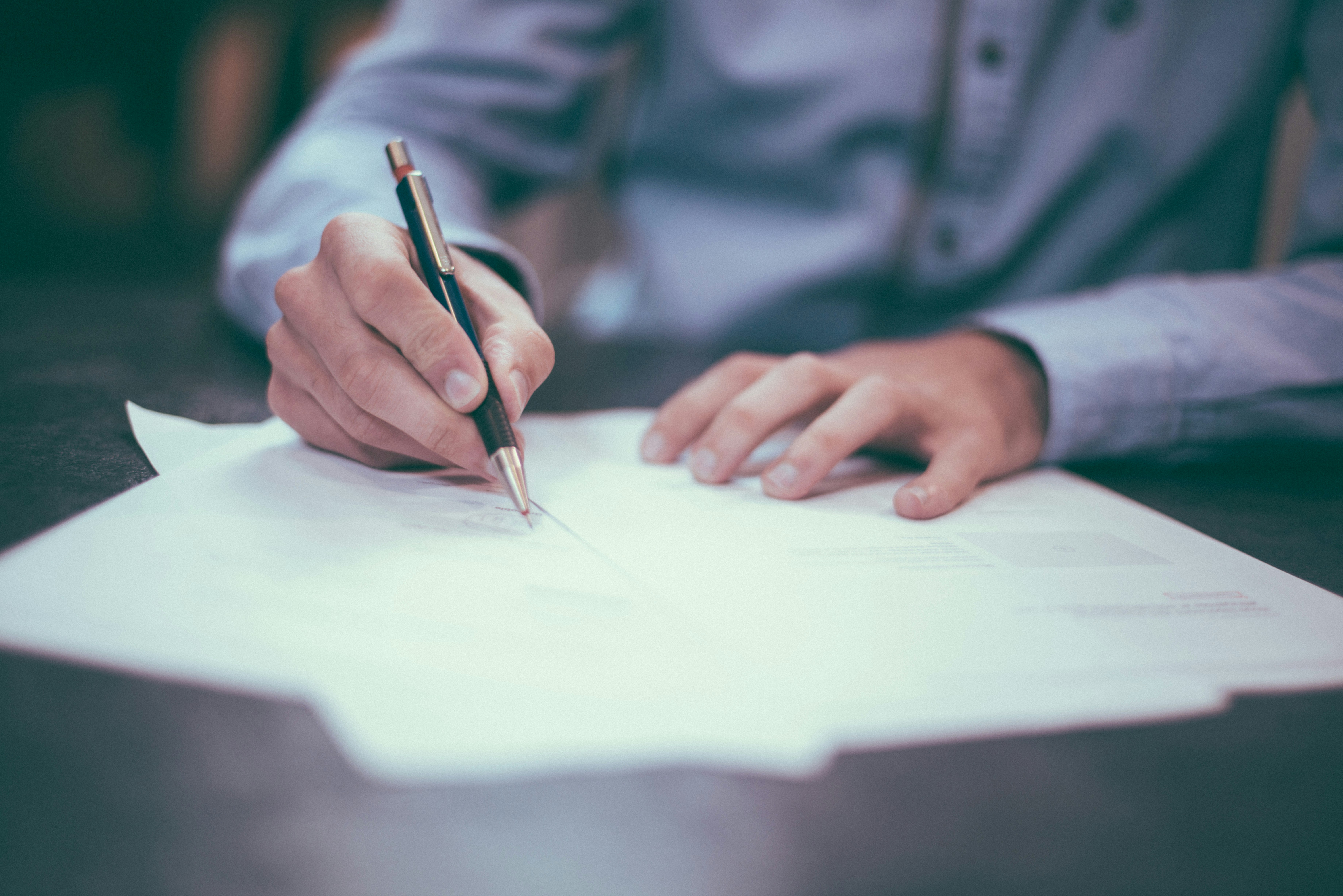 Close-up of hands signing paperwork at a desk